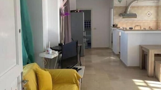 A room with a yellow sofa, a small table, a TV, and a kitchenette with a sink and cabinets. - Peaceful haven by the sea, a stone's throw from the town center 🌊 (Hammamet)