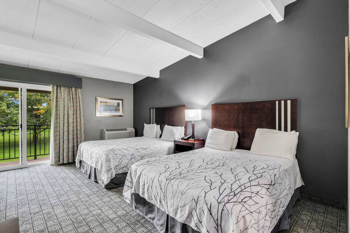 A hotel room with two beds, a large window with a view of greenery, a ceiling with a unique design, and a modern lamp.