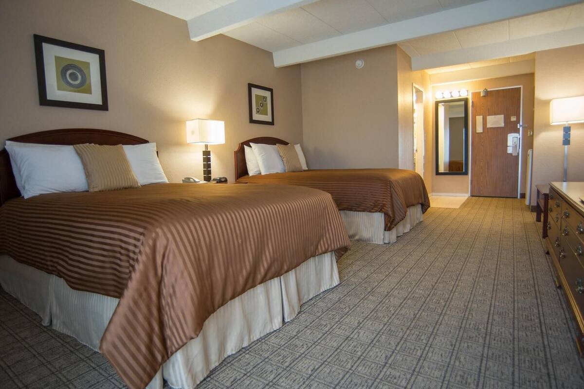 A hotel room with two beds, a desk, a mirror, and a door leading to a bathroom.