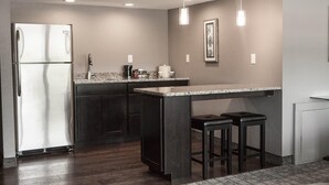 A modern kitchen with a stainless steel refrigerator, dark cabinetry, granite countertops, and pendant lighting. - Red Lion Inn & Suites Urbana (Urbana)