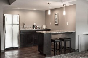 A modern kitchen with a stainless steel refrigerator, dark cabinetry, granite countertops, and pendant lighting.