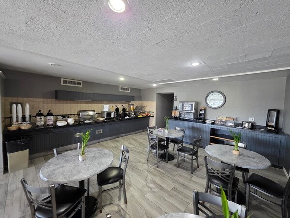 A modern cafe with round tables, chairs, a coffee station, and a clock on the wall.