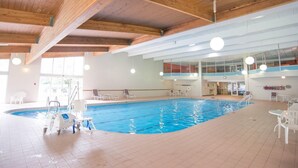 An indoor swimming pool with a wooden ceiling, clear glass walls, and a poolside area with chairs and a pool maintenance cart. - Red Lion Inn & Suites Urbana (Urbana)