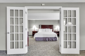 A hotel room with a large bed, two bedside lamps, a wooden headboard, and a carpeted floor.
