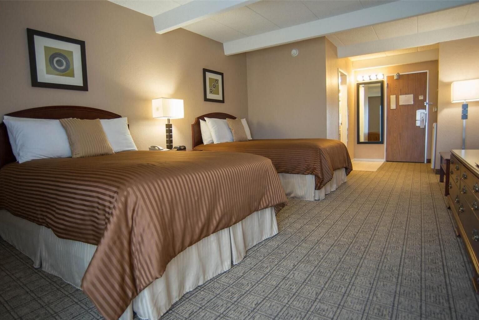 A hotel room with two beds, a dresser, a lamp, and a door leading to a hallway.