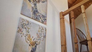Deux tableaux représentant des cerfs sont accrochés à un mur, le plafond est en bois et une chaise en bois se trouve dans un coin.