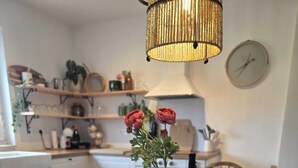 Une table à manger dressée avec des assiettes, des verres et des couverts, un vase rempli de fleurs et un luminaire suspendu dans une cuisine.
