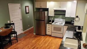 Una cocina con suelo de madera, armarios blancos, electrodomésticos de acero inoxidable y un comedor con mesa y sillas.