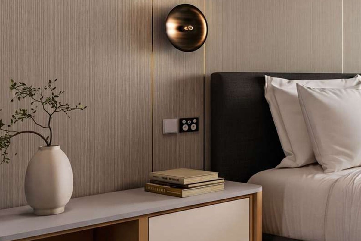 A modern bedroom with a bed, bedside table, vase, books, and a wall-mounted light fixture.