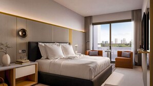 Een moderne slaapkamer met een groot bed, nachtkastjes, een stoel, een klein tafeltje met een lamp en een uitzicht op de stad door grote ramen.