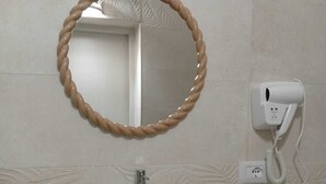A bathroom with a round mirror, a white sink, a handheld hair dryer, and a small plant on the counter. - Antonella's Suites (Taranto)
