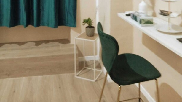 A room with teal curtains, a white console table with a plant, a green chair, and a white wall with a curved design. - Antonella's Suites (Taranto)