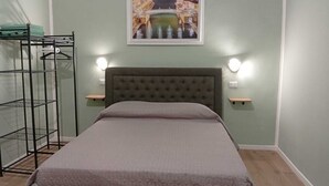 A bedroom with a bed, a nightstand, a wall-mounted shelf, and a metal rack. - Antonella's Suites (Taranto)