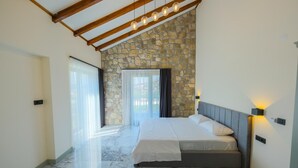 A bedroom with a stone wall, a bed with a grey headboard, and a wooden ceiling structure. - Selvi Lİfe Villa (Sapanca)
