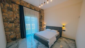 A bedroom with a stone wall, a bed with white linens, a marble floor, and a nightstand with a lamp. - Selvi Lİfe Villa (Sapanca)