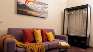 A purple sofa with red and yellow cushions, a mustard-colored throw blanket, and a small wooden side table with a book. - Napolicentrico (Naples)