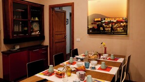A dining area with a table set for four, featuring a variety of dishes, glasses, and a painting of a market scene on the wall. - Napolicentrico (Naples)