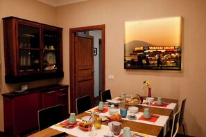 A dining area with a table set for four, featuring a variety of dishes, glasses, and a painting of a market scene on the wall. - Napolicentrico (Naples)