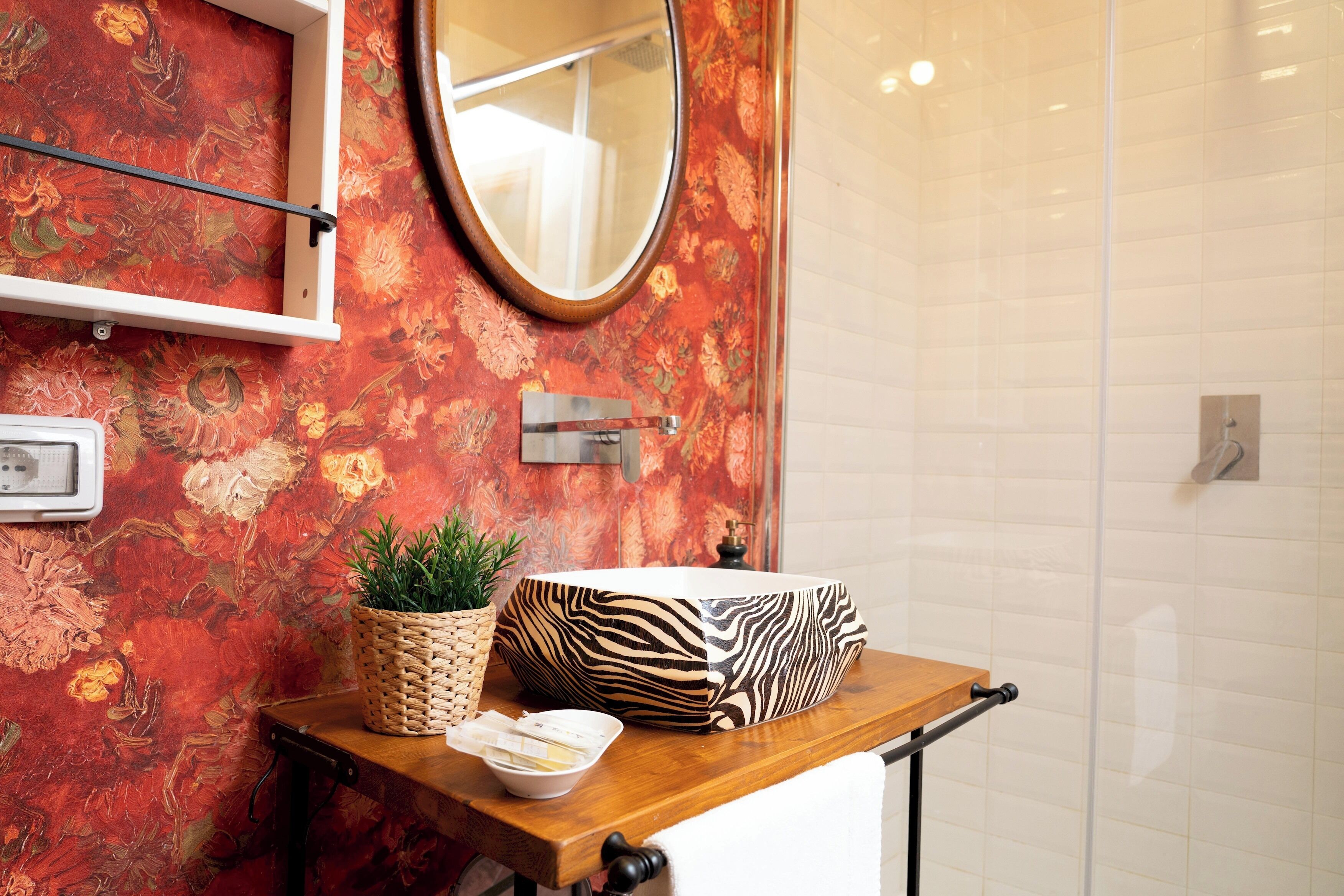 A bathroom with a floral wallpaper, a mirror, a wooden vanity, a zebra-patterned tray, a woven basket, and a potted plant.