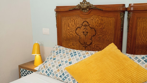 A bed with a patterned pillow, a yellow pillow, and a wooden headboard. - Napolicentrico (Naples)