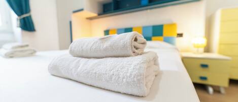 A neatly made bed with a folded white towel, a bedside table with a lamp, and a blue and yellow checkered wall.