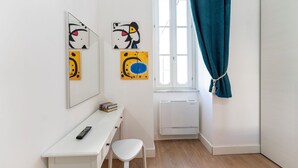 A room with a white desk, a white chair, a radiator, and two abstract paintings on the wall. - Casa di Andrea (Naples)