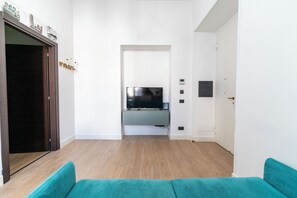 A modern living room with a flat-screen TV mounted on a wall, a wooden floor, and a teal sofa. - Casa di Andrea (Naples)