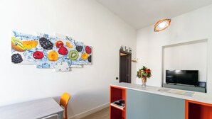 A modern kitchen with a dining area, a TV, and a fruit-themed wall art. - Casa di Andrea (Naples)