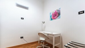 Een wit bureau met een stoel, een wandairconditioner, een afbeelding van een roze bloem en een prikbord met tekst erop.