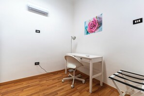 A white desk with a chair, a wall-mounted air conditioner, a picture of a pink flower, and a blackboard with writing. - Via Lanzieri 38 (Naples)
