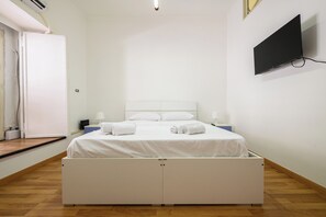 A neatly made bed with white linens and towels, a flat-screen TV mounted on the wall, and a wooden floor. - Via Lanzieri 38 (Naples)