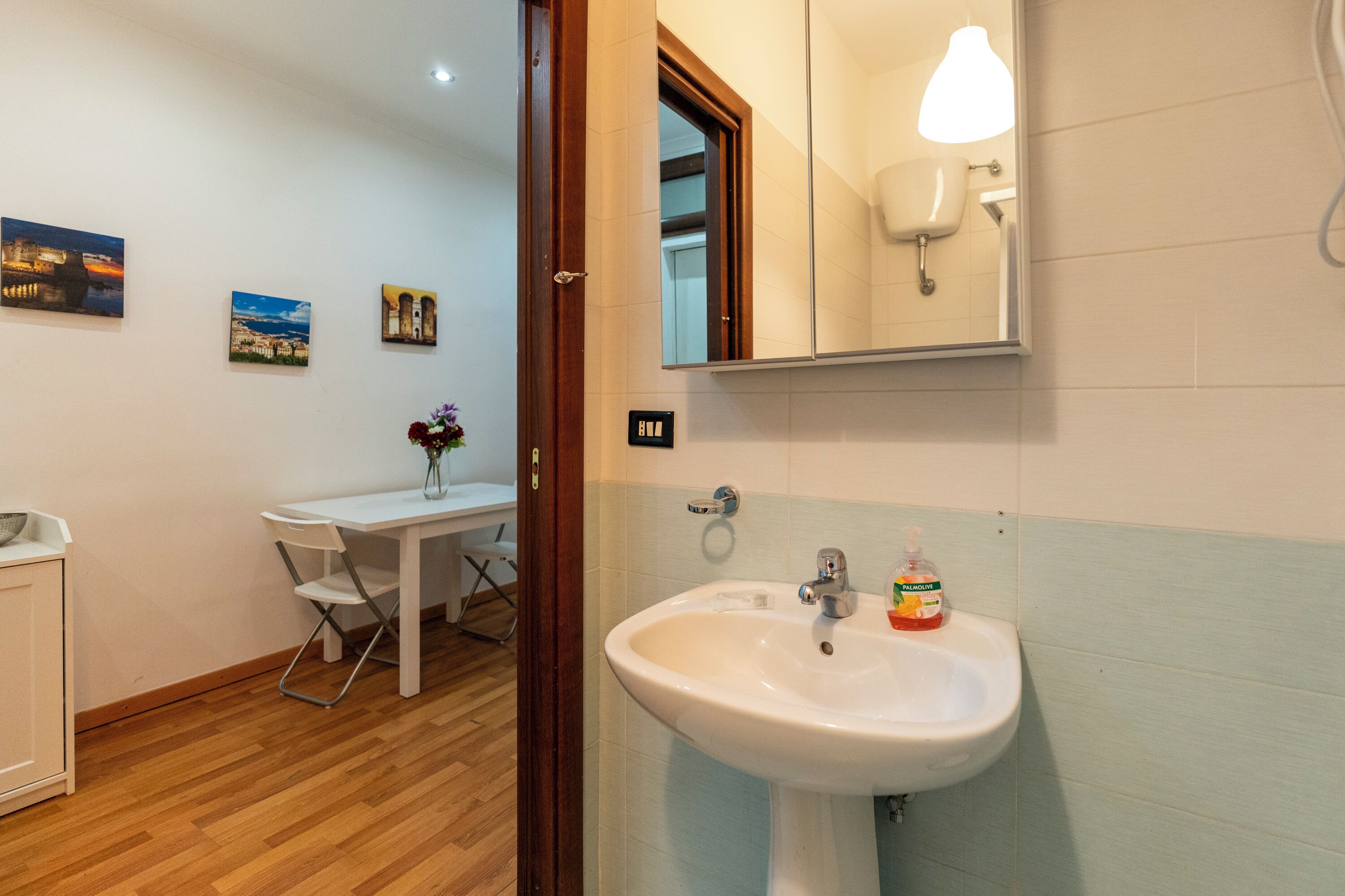 Een badkamer met een wastafel, spiegel en een klein tafeltje met stoelen.