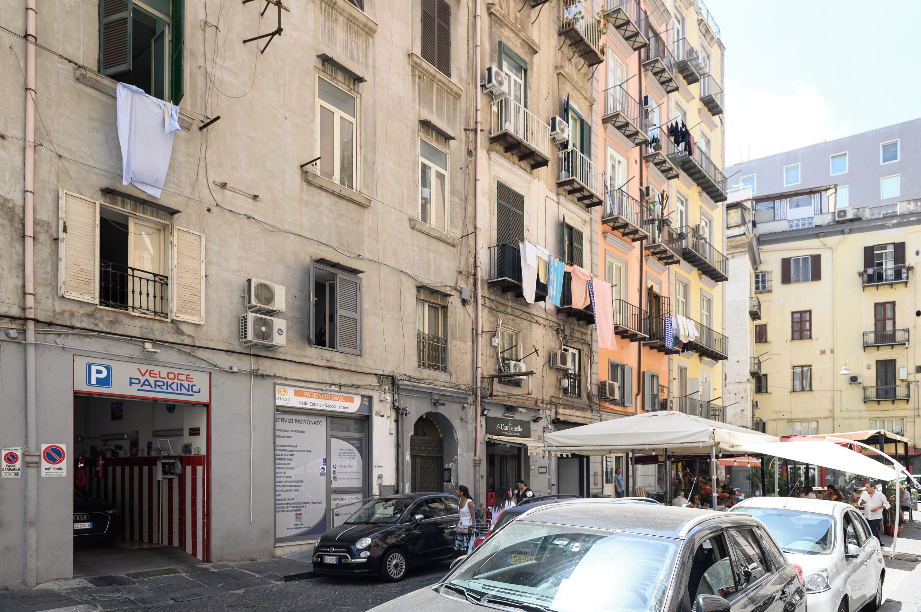 A street with parked cars, a parking sign, and a building with a sign for 'PATRONATO ENASC'.