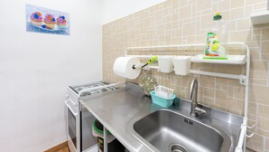 Een keuken met een roestvrijstalen spoelbak, een gasfornuis en een betegelde achterwand. Er hangen papieren handdoeken en een afwasmiddeldispenser aan de muur.