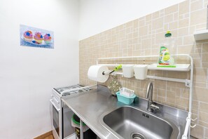 A kitchen with a stainless steel sink, a gas stove, and a tiled backsplash. There are paper towels and a dish soap dispenser on the wall. - Via Lanzieri 38 (Naples)