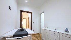 Een compacte, moderne keuken met een witte tafel en stoel, een houten vloer en een wit kastje met lades.