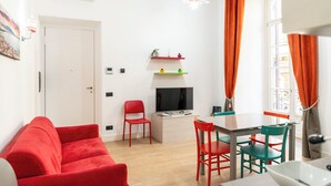A compact living space with a red sofa, a dining table with chairs, a TV, and a window with curtains. - Casa di Rosy (Naples)