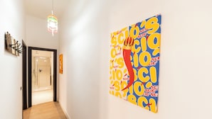 A hallway with a modern light fixture, a glass shower door, and a vibrant artwork on the wall. - Casa di Rosy (Naples)