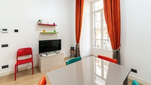 A modern living room with a flat-screen TV, a red chair, a small table, and a window with orange curtains. - Casa di Rosy (Naples)
