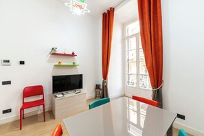 A modern living room with a flat-screen TV, a red chair, a small table, and a window with orange curtains. - Casa di Rosy (Naples)