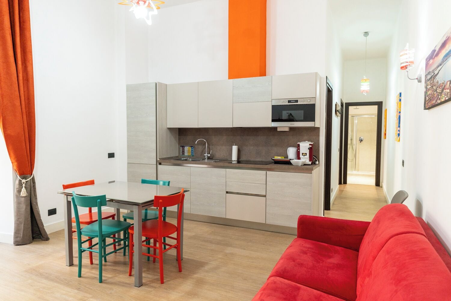 Un espace de vie compact comprenant un coin cuisine, un coin repas avec des chaises dépareillées et un canapé rouge.