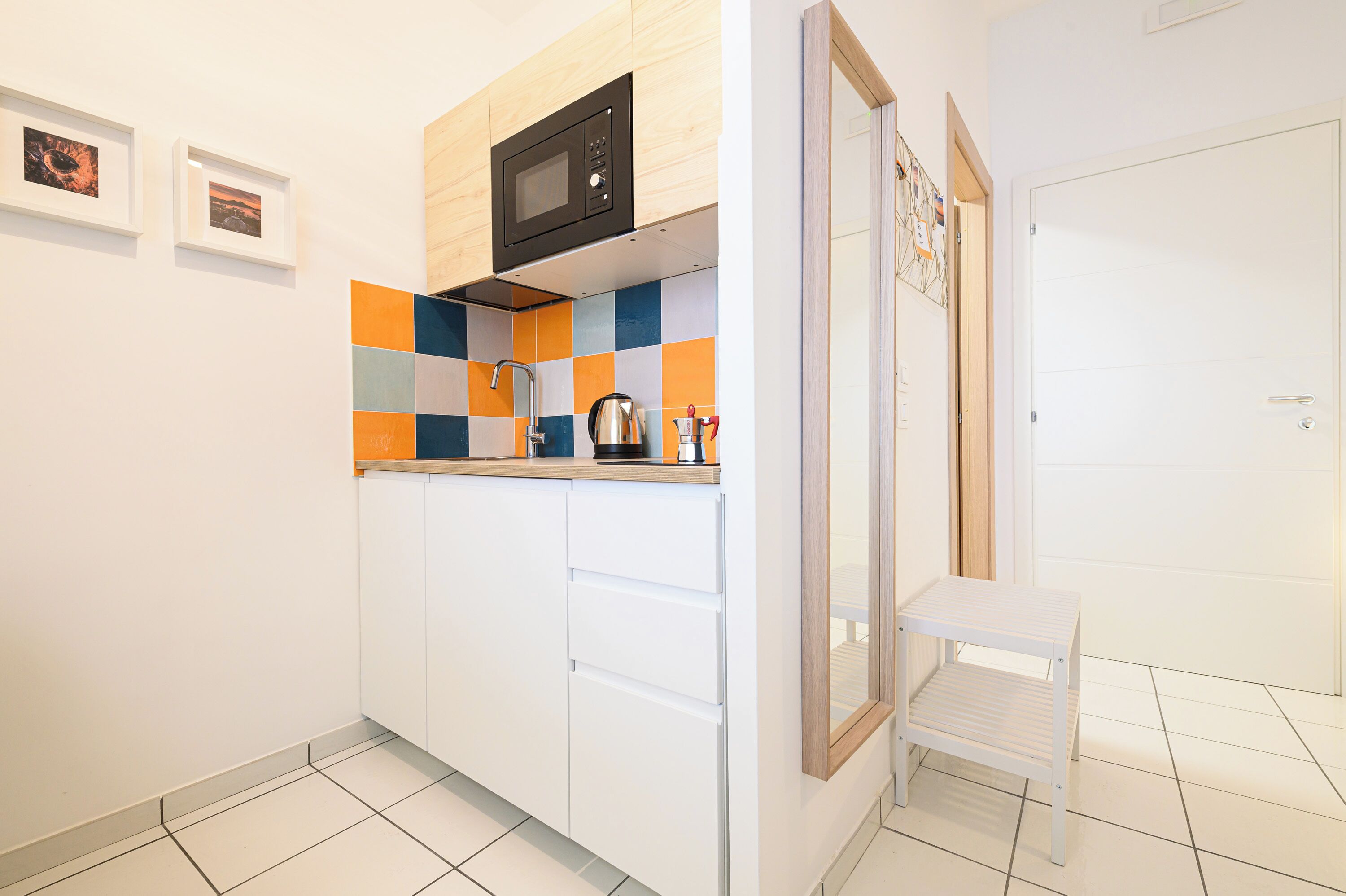 Cocina compacta con armarios blancos, microondas, cafetera y un taburete pequeño blanco.
