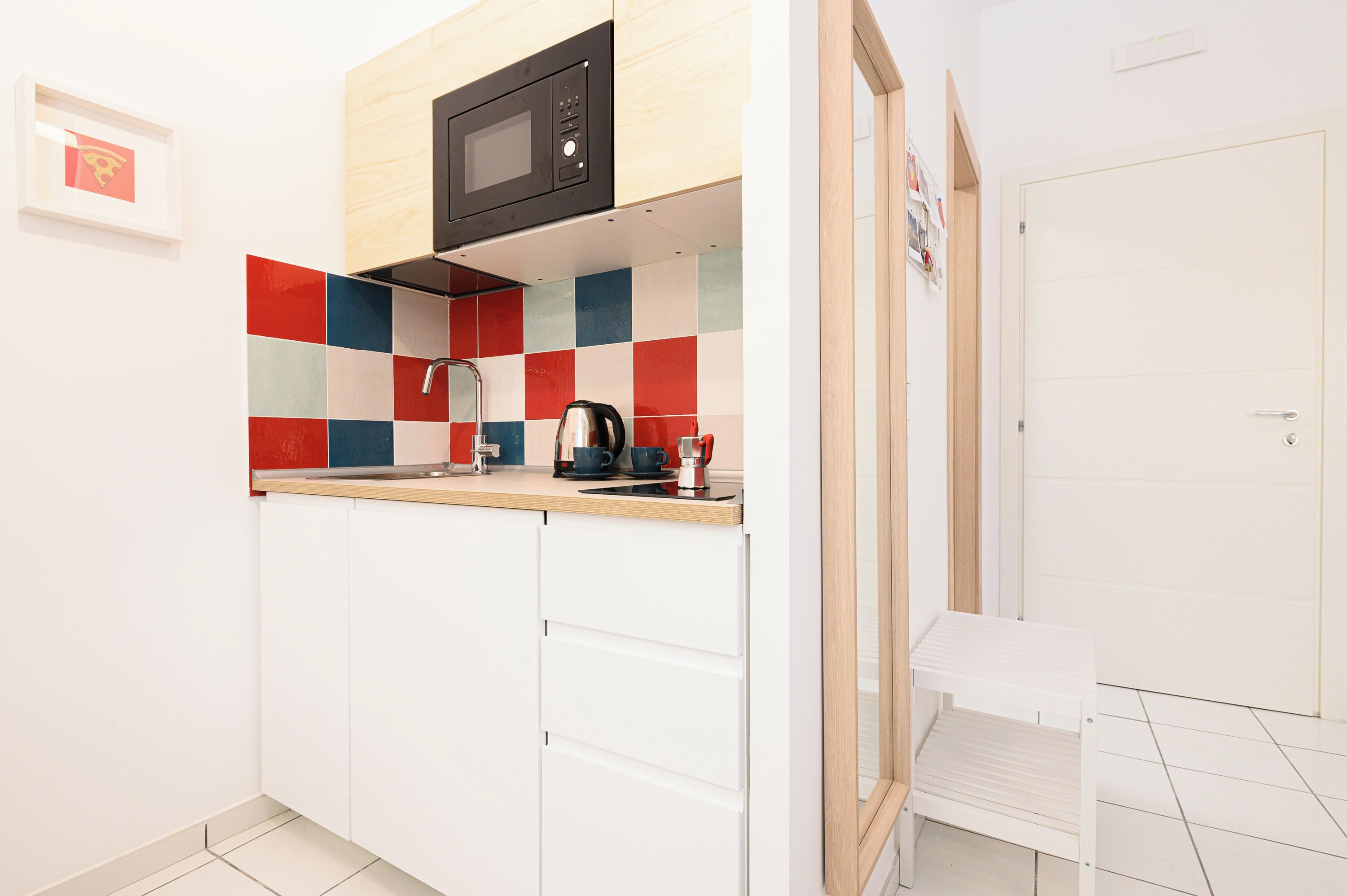 A compact kitchen with a microwave, kettle, and coffee maker on the countertop.