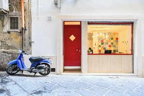 A red door with a small window, a blue scooter parked in front, and a colorful tiled wall visible through the door. - L'Aurora Apartments (Naples)