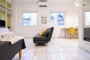 A modern room with a grey sofa, a dining table with yellow chairs, and a TV on a white cabinet. - L'Aurora Apartments (Naples)