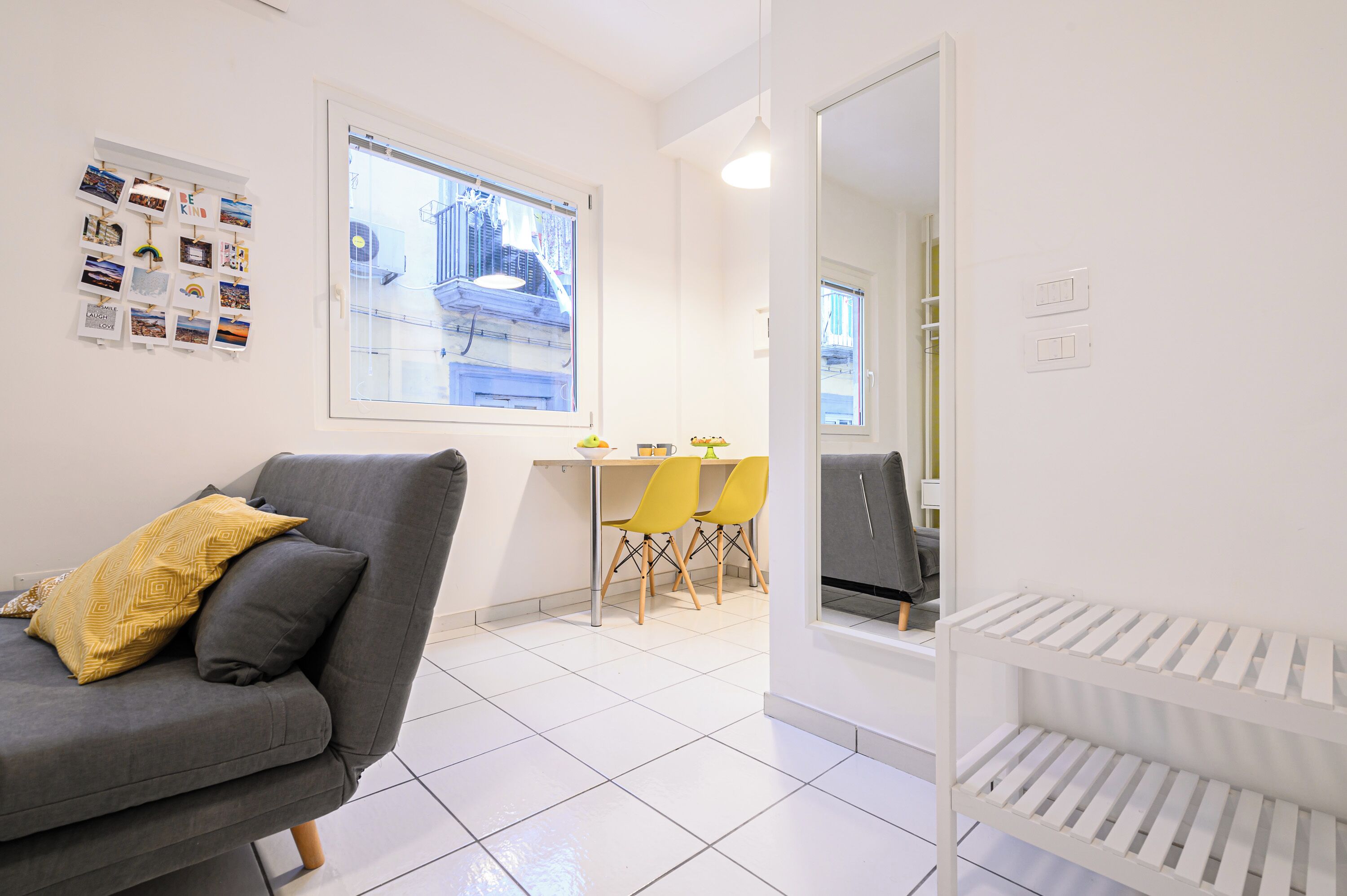 Ein modernes Wohnzimmer mit einem grauen Sofa, gelben Kissen, einem Essbereich mit gelben Stühlen und einer weißen Heizung.