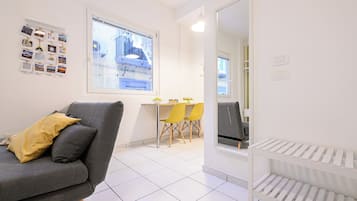 Ein modernes Wohnzimmer mit einem grauen Sofa, gelben Kissen, einem Essbereich mit gelben Stühlen und einer weißen Heizung.