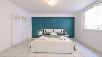 Een moderne hotelkamer met een groot bed, een muur in teal kleur en een raam dat natuurlijk licht binnenlaat.