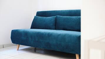 Un sofá azul con patas de madera en una habitación con paredes blancas y suelo de baldosas.