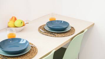 A dining table with two blue plates, a glass of orange juice, and a bowl of fruit.
